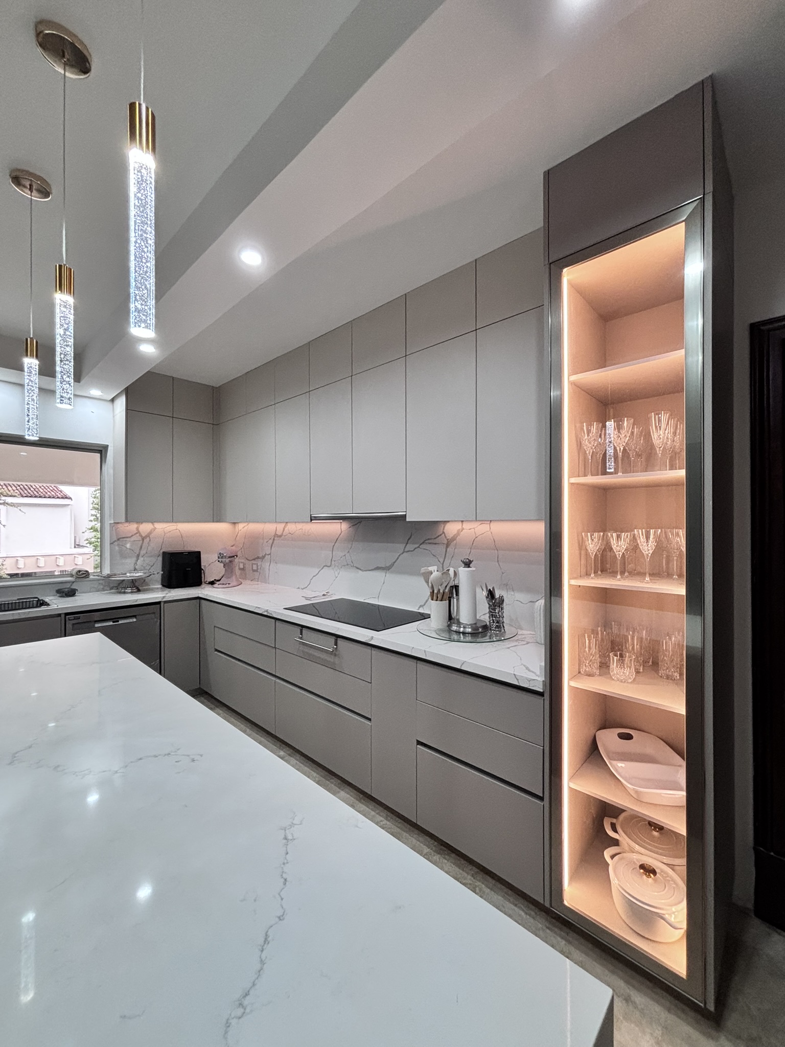 Cocina moderna en Monterrey con isla central, gabinetes en tono gris, cubierta tipo mármol e iluminación integrada